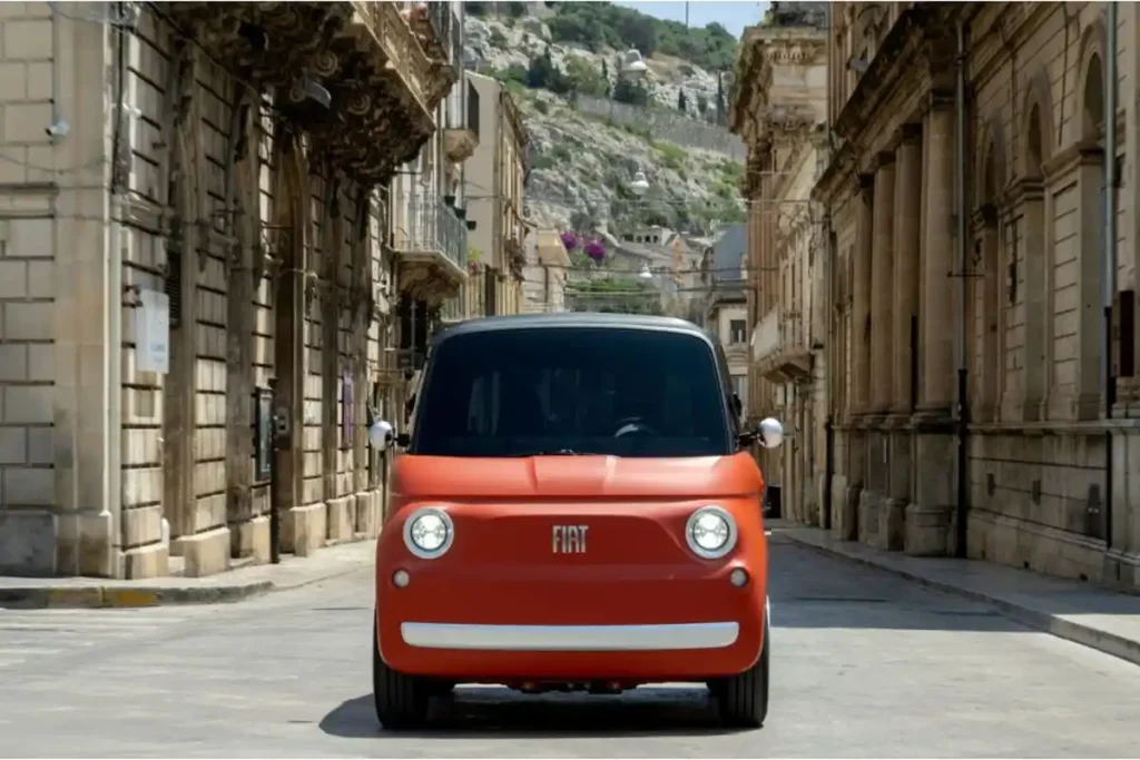 Fiat Topolino color corallo vista frontale in una strada cittadina